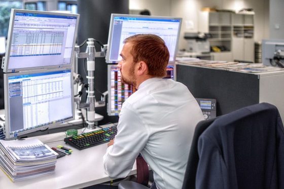 Ein Fondsmananger sitzt an seinem Schreibtisch und beobachtet die Börsenaktivitäten auf drei Bildschirmen vor sich.
