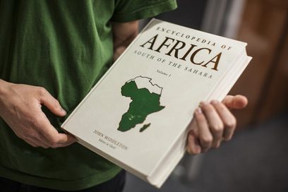 Ein Mann in grünem T-Shirt hält eine Enzyklopädie von Afrika in seinen Händen. Auf dem Titel ist der Umriss des afrikanischen Kontinents abgebildet.